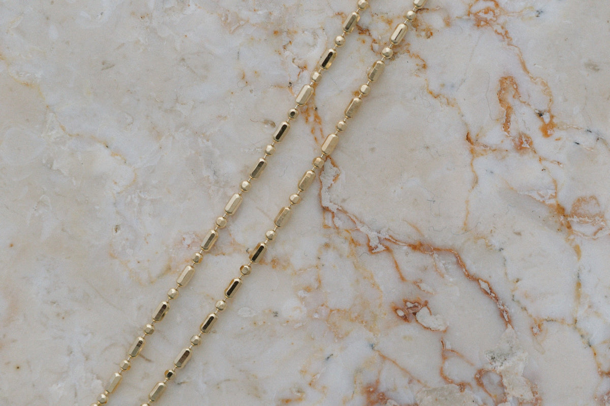 Bar & Tube Petite Chain by Lane & Kate in 14kt yellow gold, close up on marble