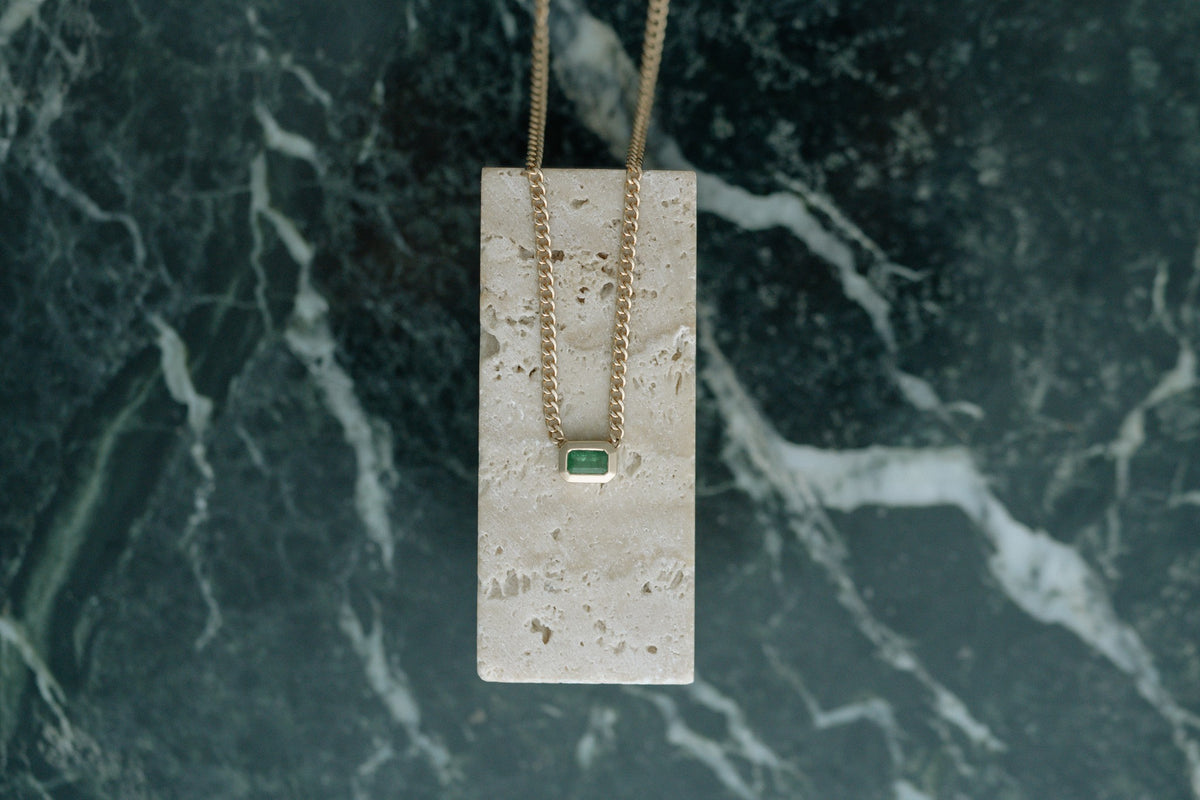 Zoe Chicco Emerald Bezel Set Curb Chain in 14kt yellow gold draped over travertine on green marble