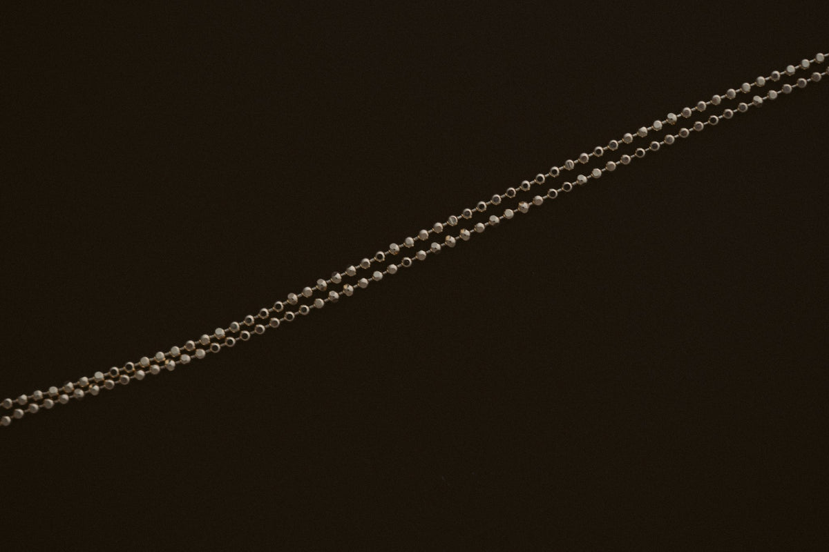 BB Ball Chain in 10kt yellow gold, a dainty diamond cut bead chain on a dark background