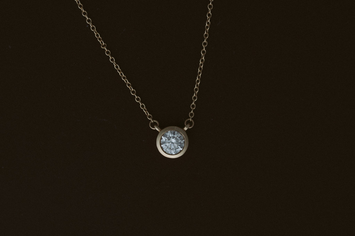 Heirloom Deity Pendant, a bezel set round diamond on a 14kt yellow gold cable chain on a dark background