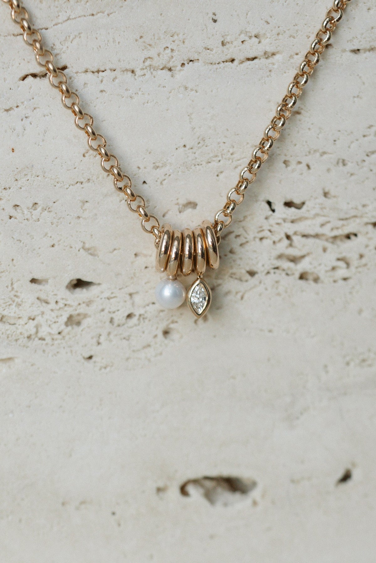 Zoe Chicco Mixed Rings Diamond Necklace in 14kt yellow gold with five gold rings, a round diamond and a marquise diamond on travertine