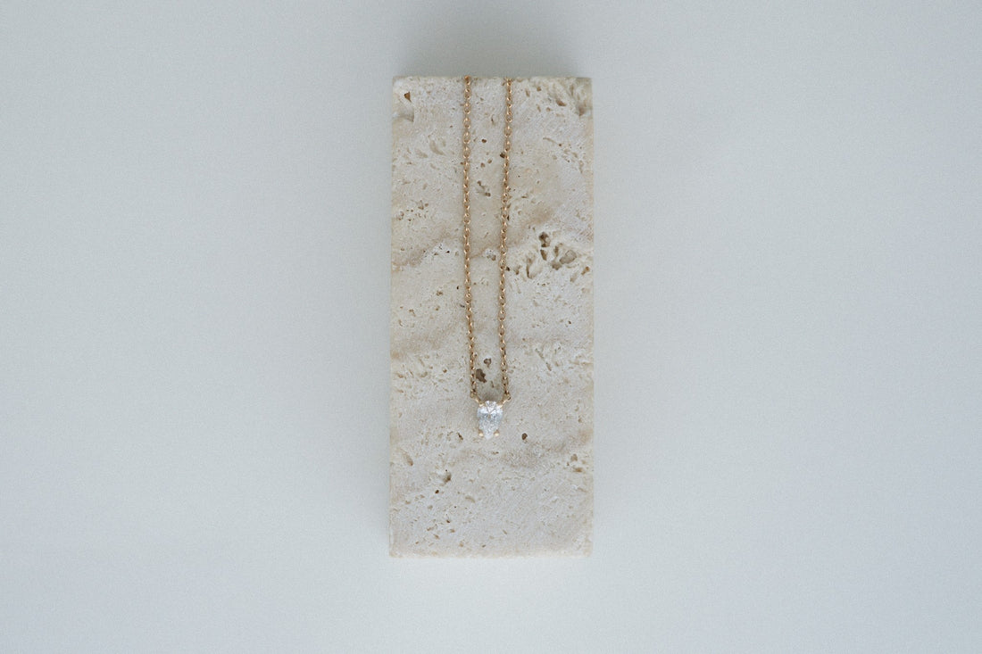 Tear of Cupid Pendant draped over a travertine block
