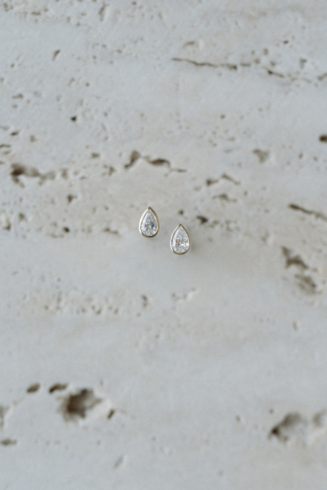 Pear Dew Drops by Lane &amp; Kate, bezel set pear diamond studs styled on travertine