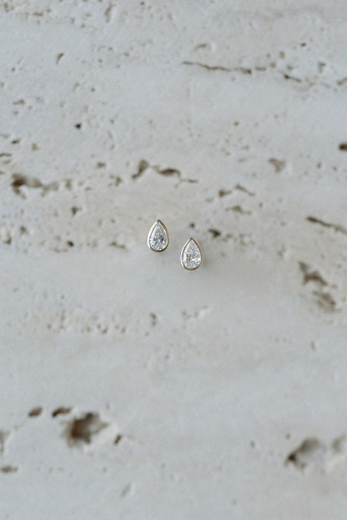 Pear Dew Drops by Lane &amp; Kate, bezel set pear diamond studs styled on travertine