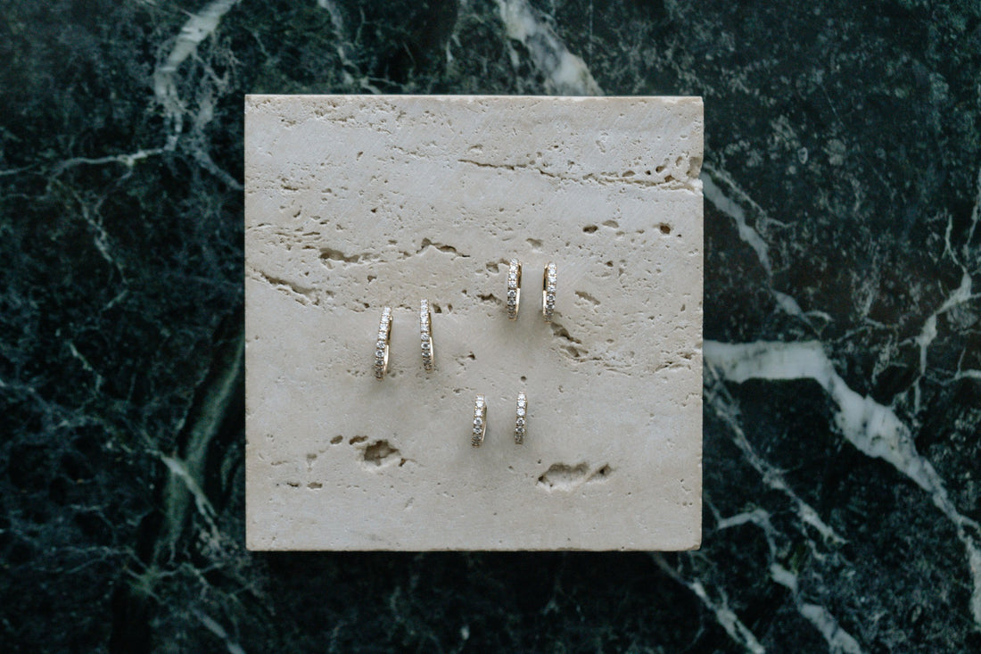 Mid Classic Diamond Huggies by Lane &amp; Kate in 14kt yellow gold, styled on travertine and green marble