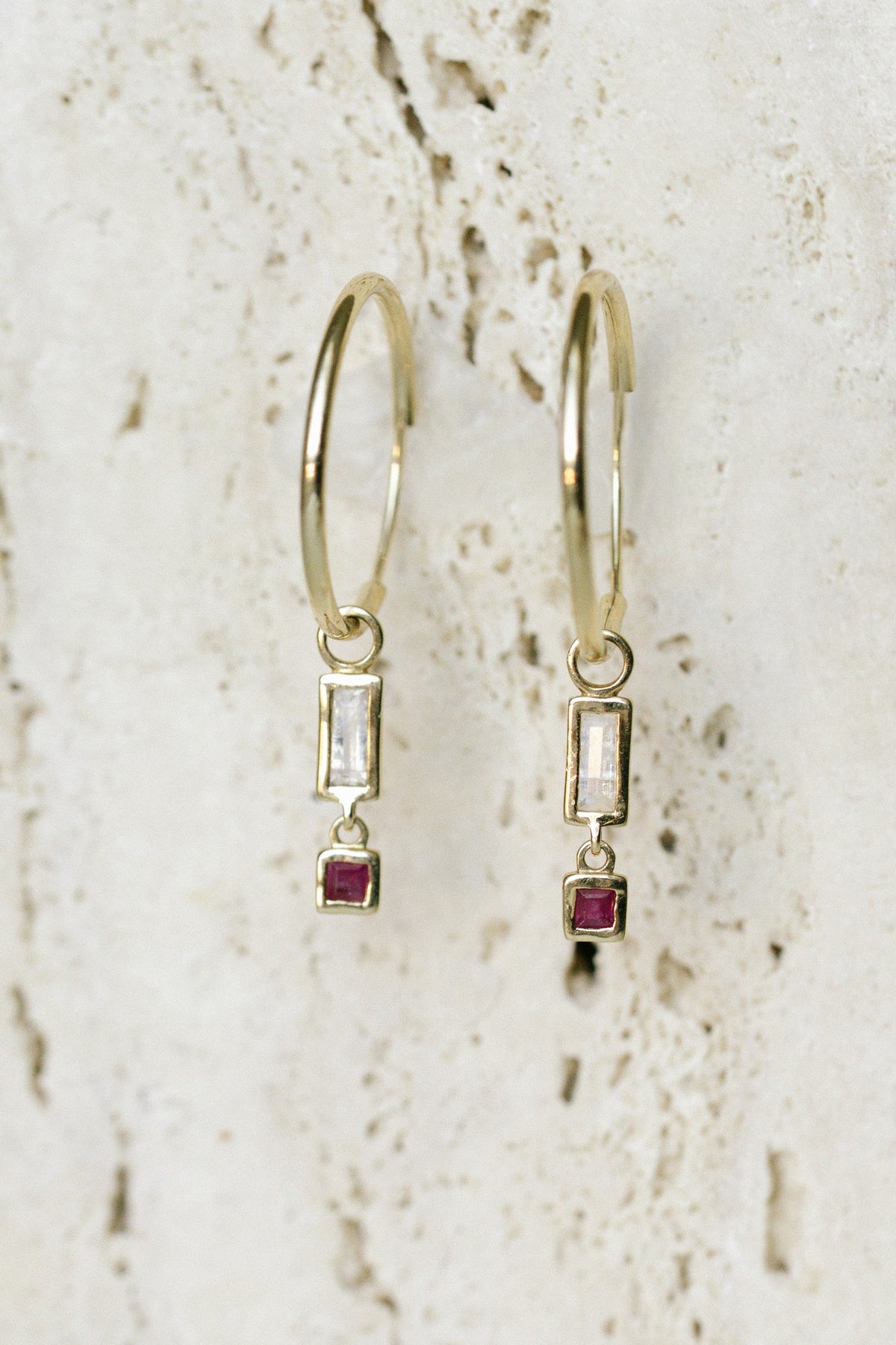 Bluboho Blessings Abound Moonstone Earring Charms with carved moonstone and ruby on 14kt yellow gold hoops, hanging on travertine