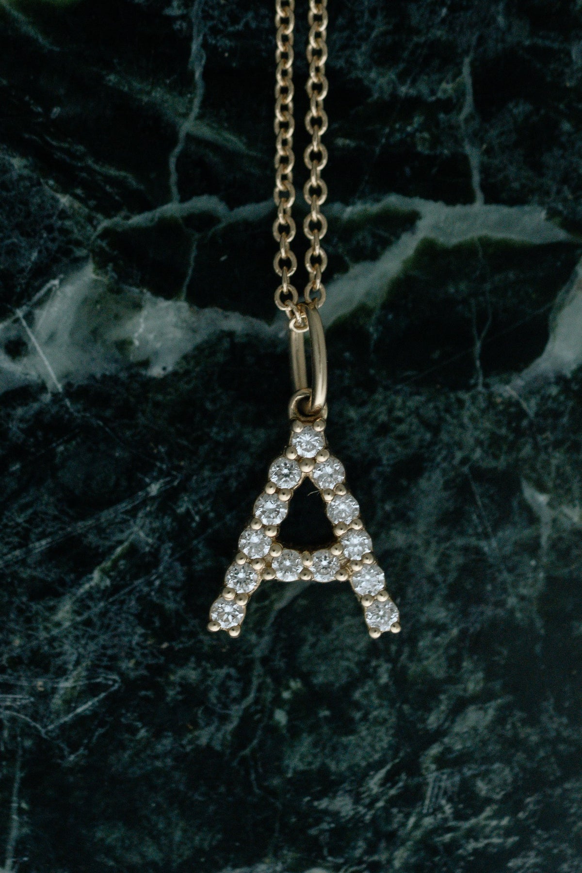 Diamond Initial Necklace, diamond letter A pendant in 14kt yellow gold hanging over green marble