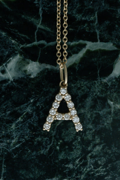 Diamond Initial Necklace, diamond letter A pendant in 14kt yellow gold hanging over green marble