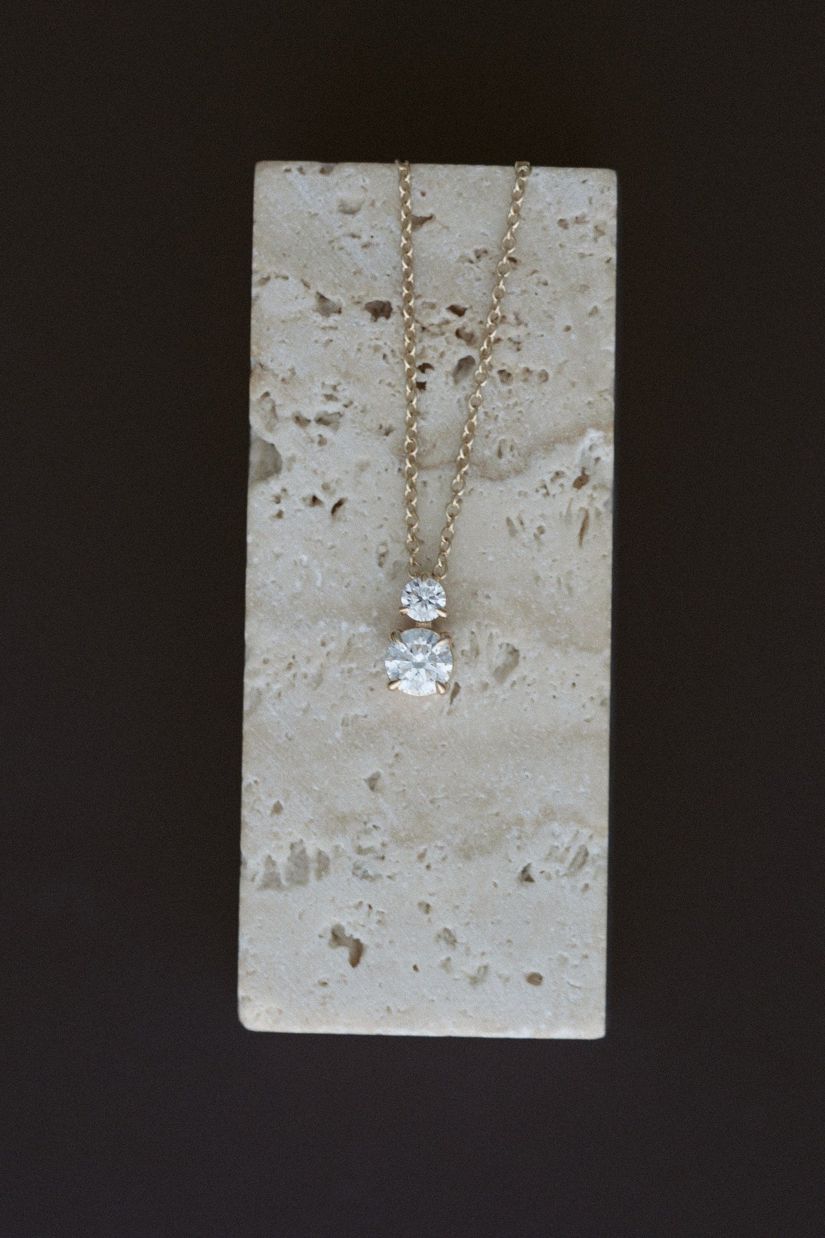 Diamond Horizon Pendant in 14kt yellow gold, a claw prong round diamond with a petite diamond above, draped over travertine