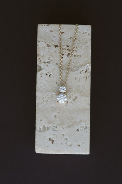 Diamond Horizon Pendant in 14kt yellow gold, a claw prong round diamond with a petite diamond above, draped over travertine