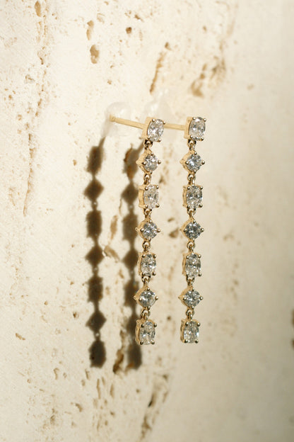 Glimmer Diamond Drops, seven stone oval and round diamond drop earrings in 14kt yellow gold hanging on travertine