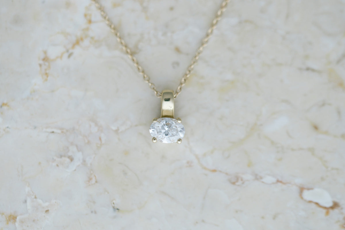 Oval Prism Necklace, a four prong oval diamond on a 14kt yellow gold cable chain on travertine