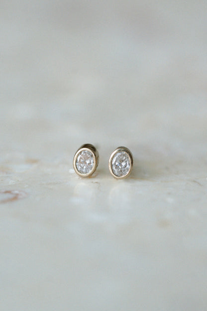Oval Damsel Studs, bezel set oval diamond earrings in 14kt yellow gold on stone, close up