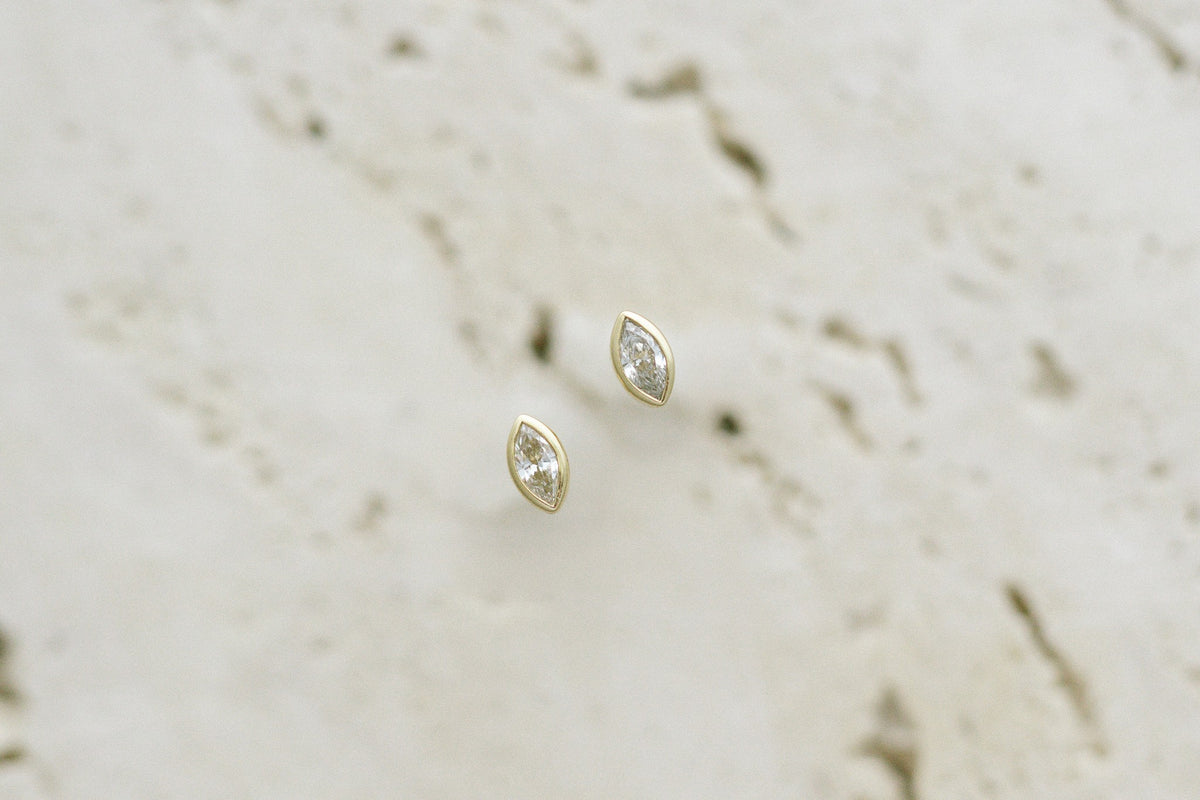 BB Marquise Dew Drops, bezel set marquise diamond studs in 14kt yellow gold on travertine